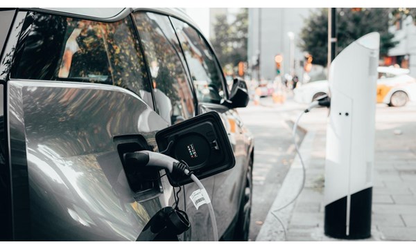 Car parked a busy urban street, plugged into an electric vehicle charging station.