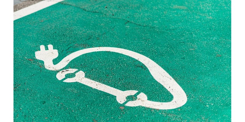 Close-up of electric vehicle charge bays green coloured asphalt, with white painted charging symbol.