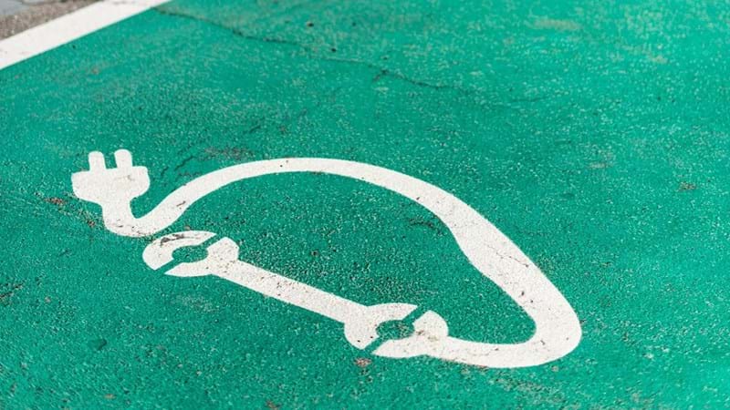 Close-up of electric vehicle charge bays green coloured asphalt, with white painted charging symbol.