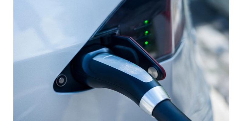 Close-up if an electrical vehicle charging cable, plugged into the side of a car.