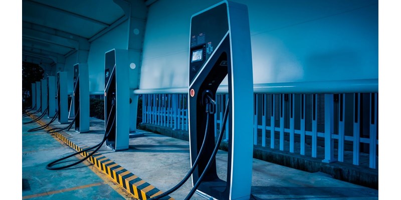 A row of modern electric vehicle charging stations, in a covered parking bay at night.