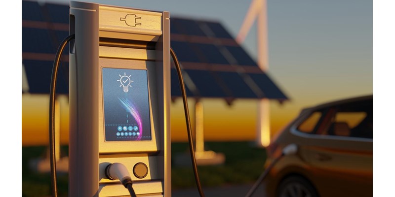 Electric car charging with wind turbines and solar panels in the background.