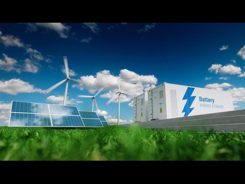 3D rendering of electricity storage units, solar panels and wind turbines, in a green field on a clear day.