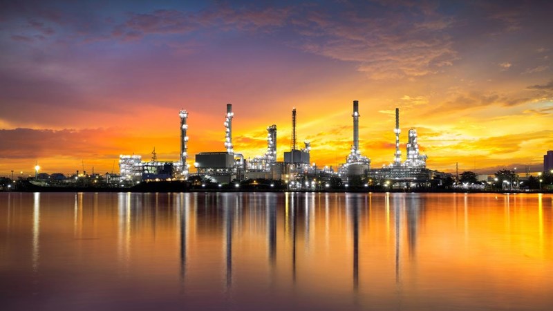 A gas refinery during an orange illuminated sunset, with reflection in the water.