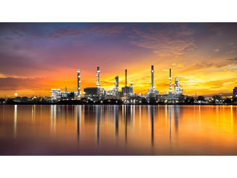 A gas refinery during an orange illuminated sunset, with reflection in the water.