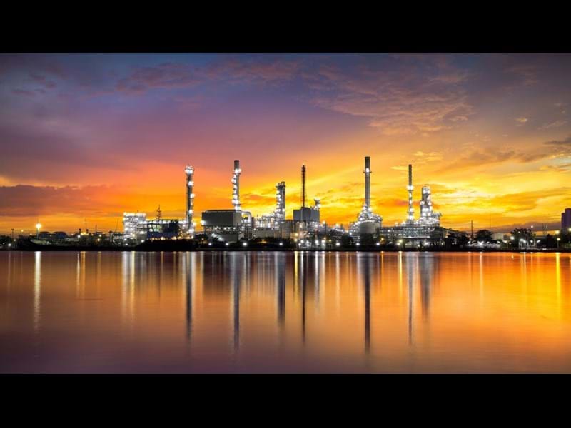 A gas refinery during an orange illuminated sunset, with reflection in the water.