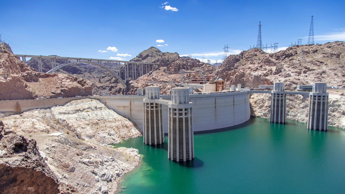 The hoover dam in Nevada, a bridge and electricity pylons on the surrounding rocky hills.