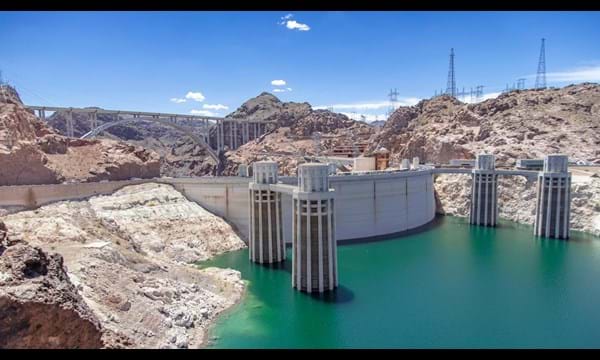 The hoover dam in Nevada, a bridge and electricity pylons on the surrounding rocky hills.