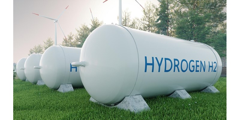 3D render of four hydrogen fuels tanks, in a tree-lined field with wind turbines to the side.