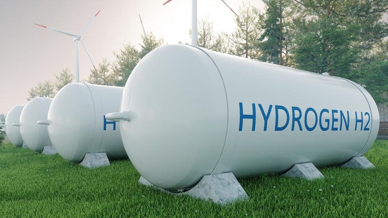 3D render of four hydrogen fuels tanks, in a tree-lined field with wind turbines to the side.