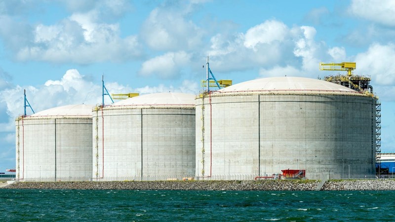 Three large LNG storage tanks, next to a body of water.