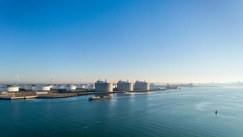 LNG tanks and wind turbines at the banks of a river.