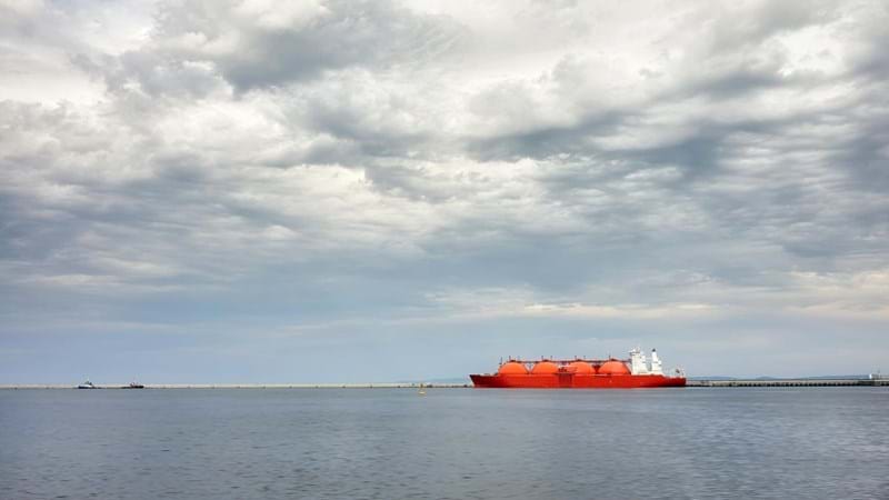 Red LNG tanker in port with stormy cloudscape.