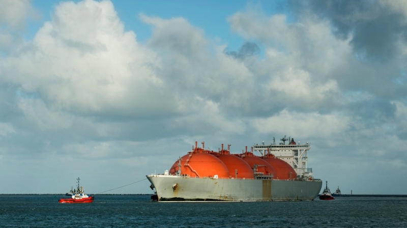 A large LNG ship in the sea, being guided by a tug and another boat in the background.
