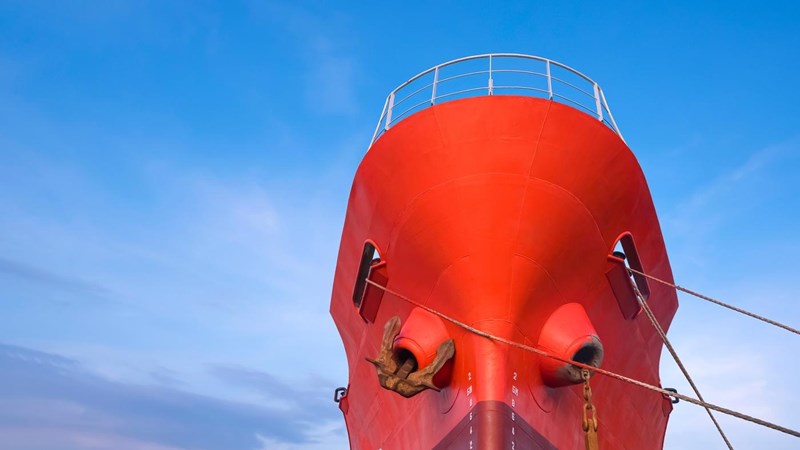Red Oil Tanker moored at port with mooring rope against blue sky background.