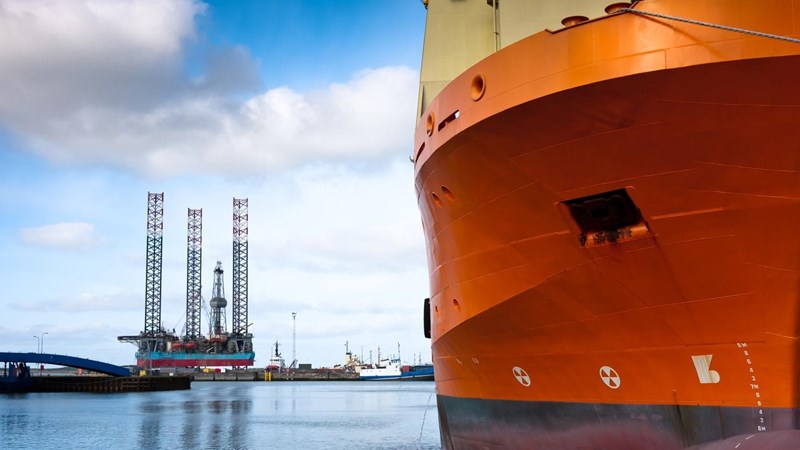 Oil rig at harbour with ship in foreground.