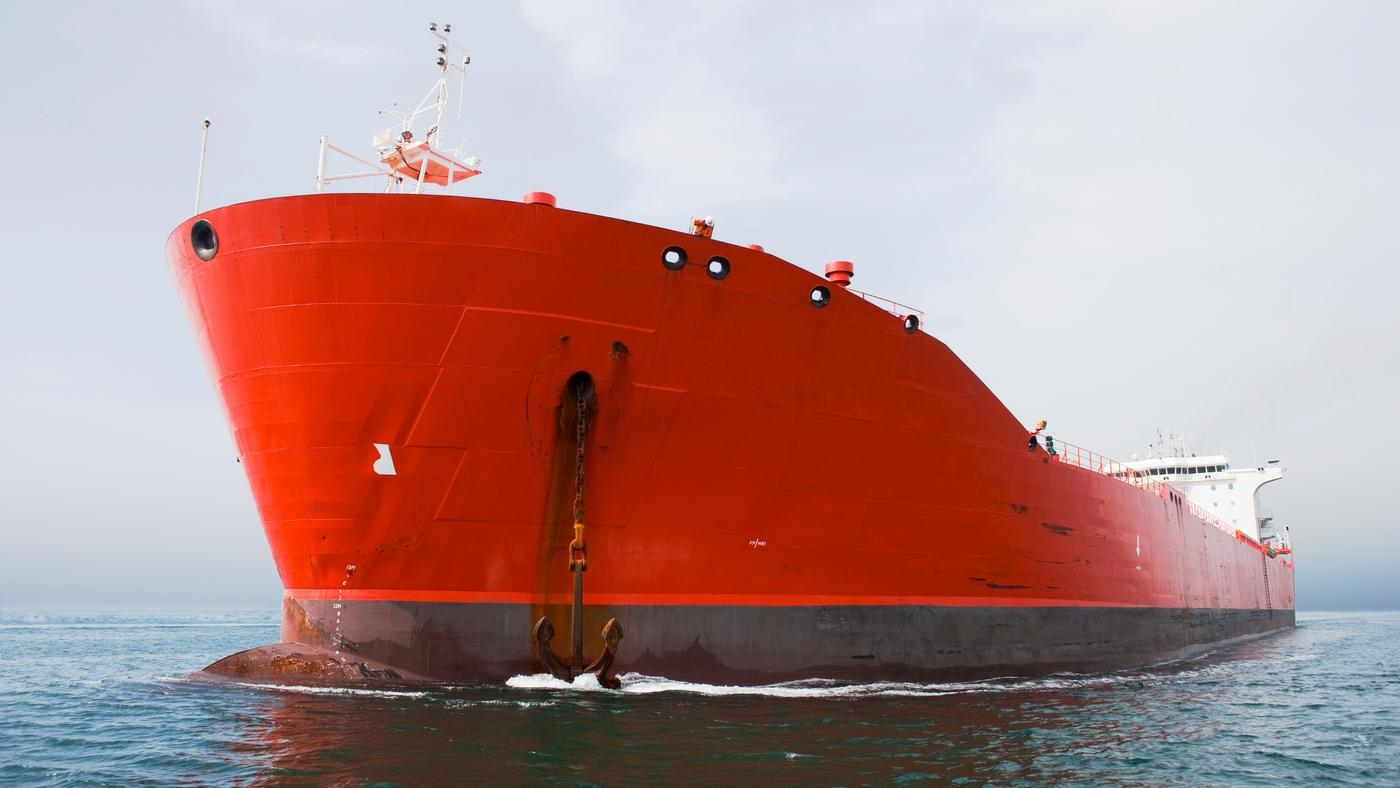 Red ship dropping anchor near port.