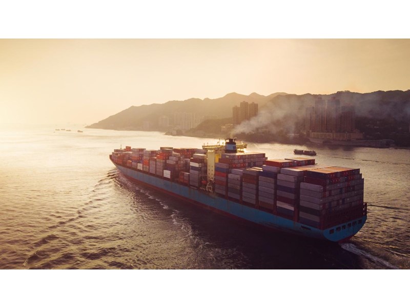 Aerial view of container ship transporting goods sailing across ocean leaving the port.