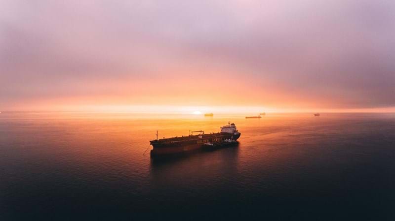 Several container ships on an open expanse of water at dusk.