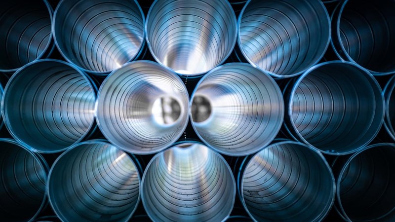 Rows of stacked metallic blue pipes.