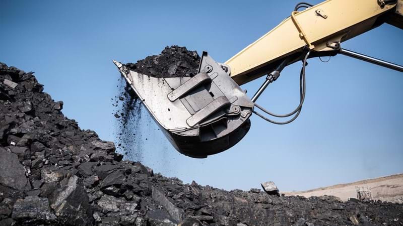 An excavator is scooping coal out of a pile.