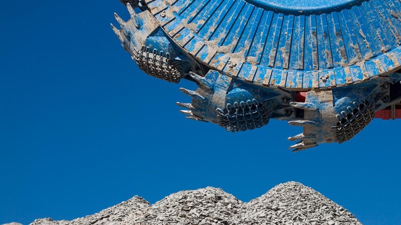 A blue excavator in the working a pile of rocks.