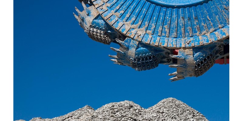 A blue excavator in the working a pile of rocks.