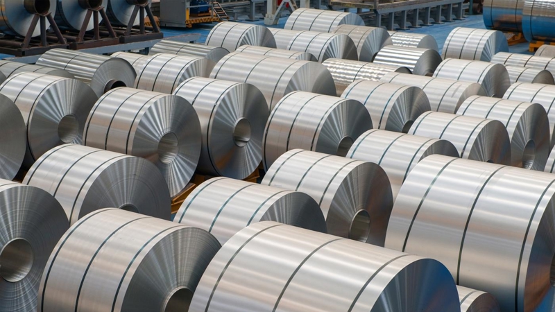 Multiple rolls of aluminium are lines up in a factory.