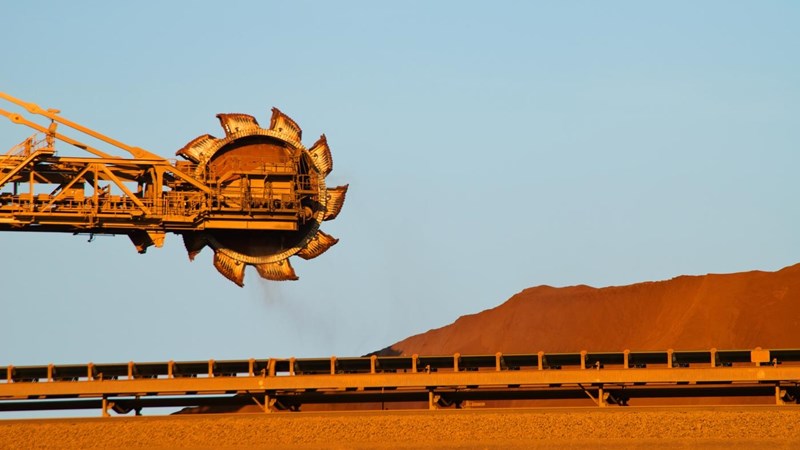 A crane is lifting a load of sand onto a conveyor belt.