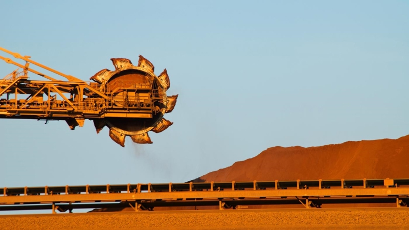A crane is lifting a load of sand onto a conveyor belt.