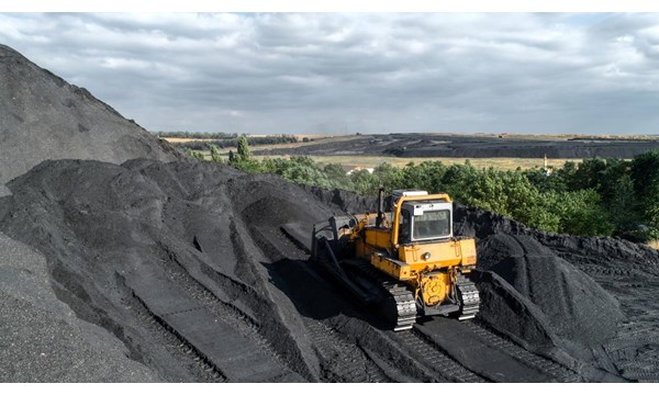 A yellow digger is mining rocks in next to rolling countryside hills.