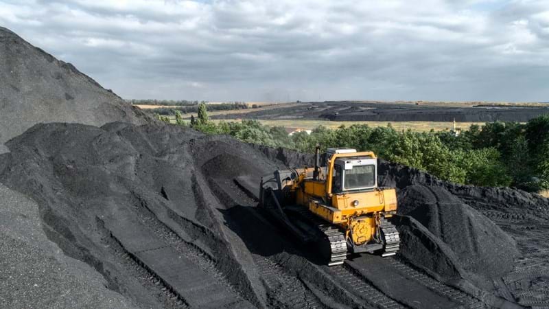 A yellow digger is mining rocks in next to rolling countryside hills.