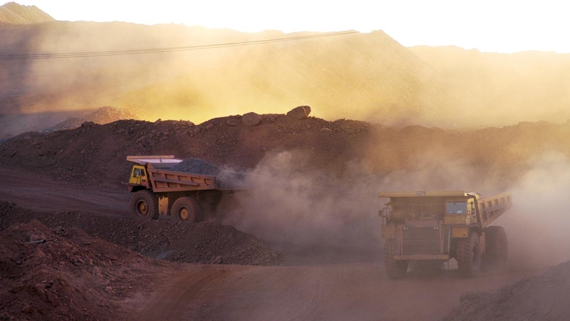 Two dump trucks driving down a dirt road in a quarry.