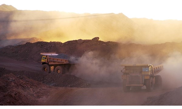 Two dump trucks driving down a dirt road in a quarry.