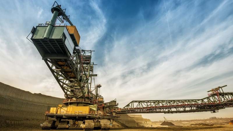 A large crane is in the middle of a quarry/mine, against a blue sky.