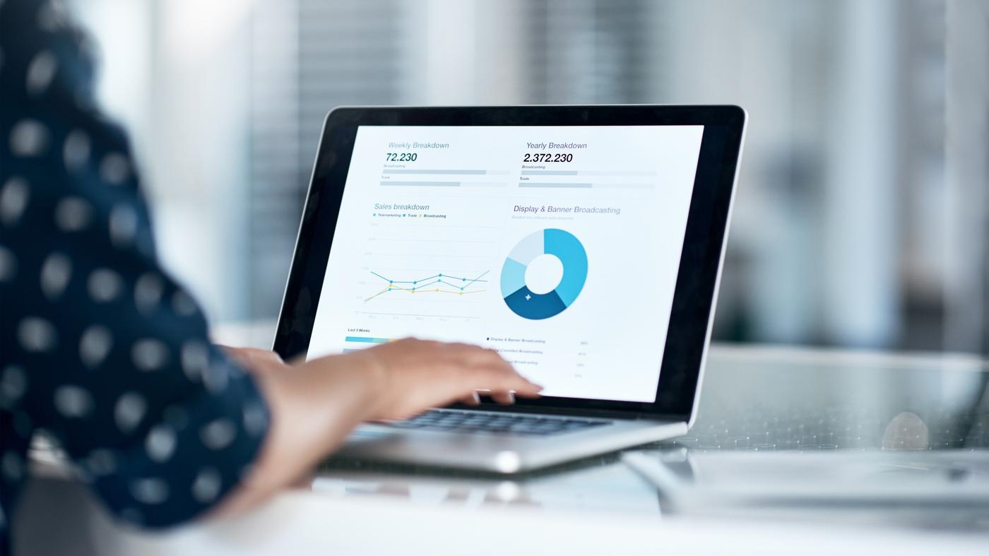 Cropped shot of a businesswoman using a laptop at her desk in a modern office, looking at data charts.