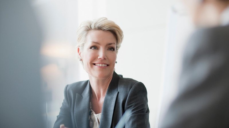 A woman in a business suit is talking to another woman in a meeting.