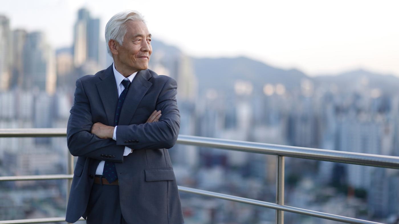 A man in a suit is standing on a balcony overlooking a city.