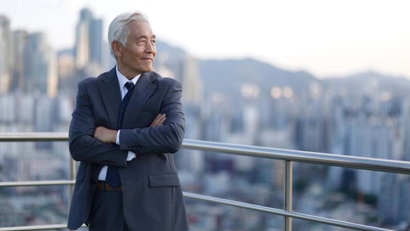 A man in a suit is standing on a balcony overlooking a city.