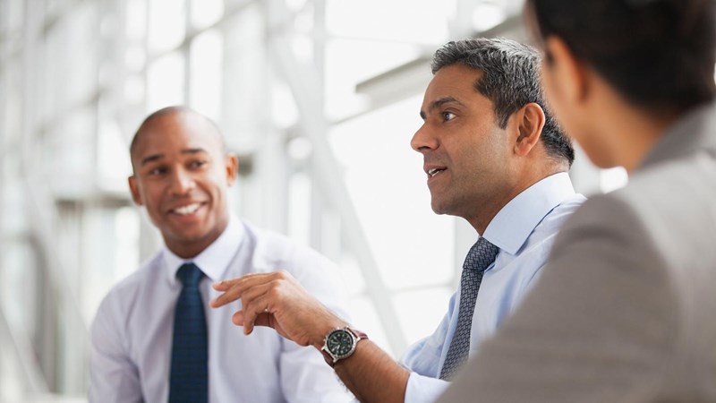 Three business people, smartly dressed, talking in an office.