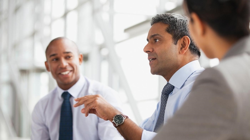 Three business people, smartly dressed, talking in an office.