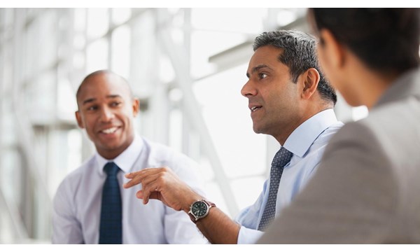 Three business people, smartly dressed, talking in an office.