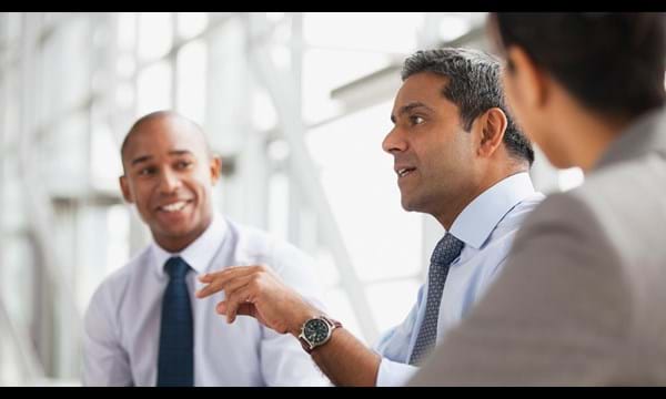 Three business people, smartly dressed, talking in an office.