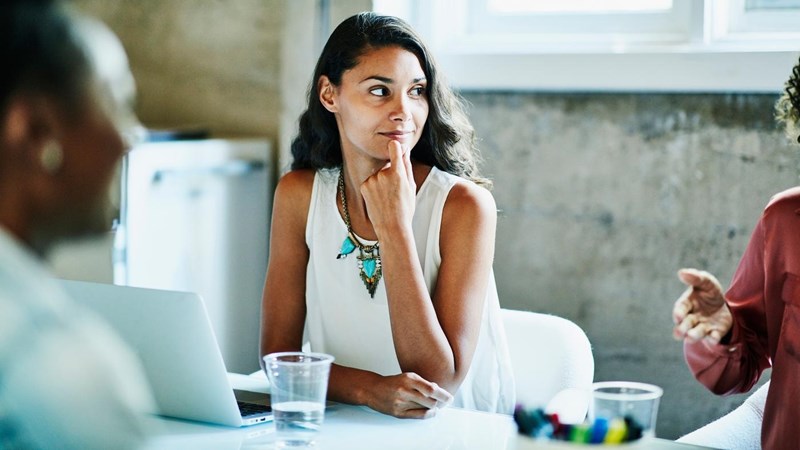 Smiling businesswoman listening to coworker during meeting in conference room.