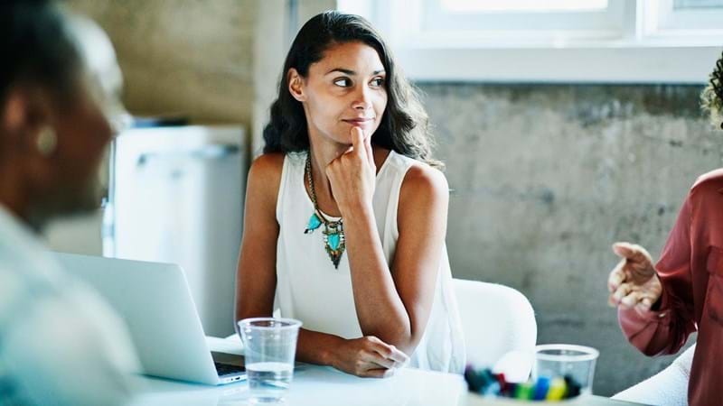 Smiling businesswoman listening to coworker during meeting in conference room.