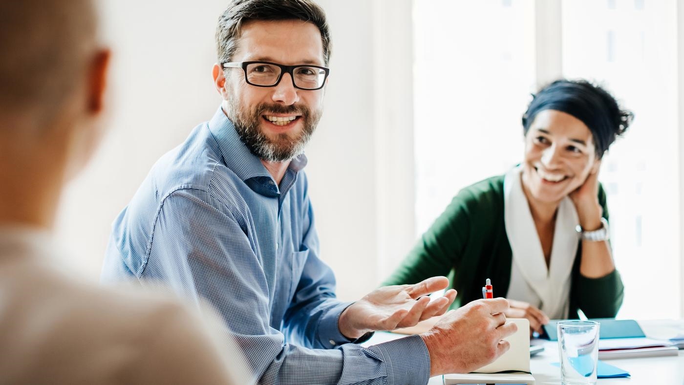 A manager sitting at a desk and talking with his employees  during a meeting at the office.