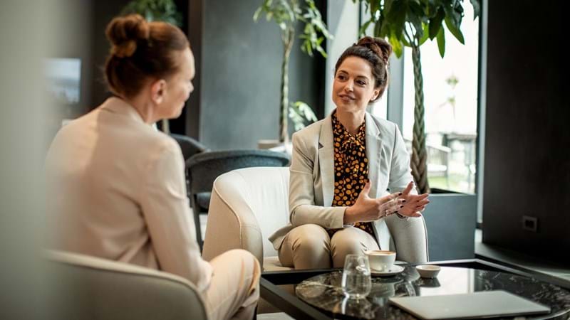 Close up of two businesswoman having coffee in an office lobby.