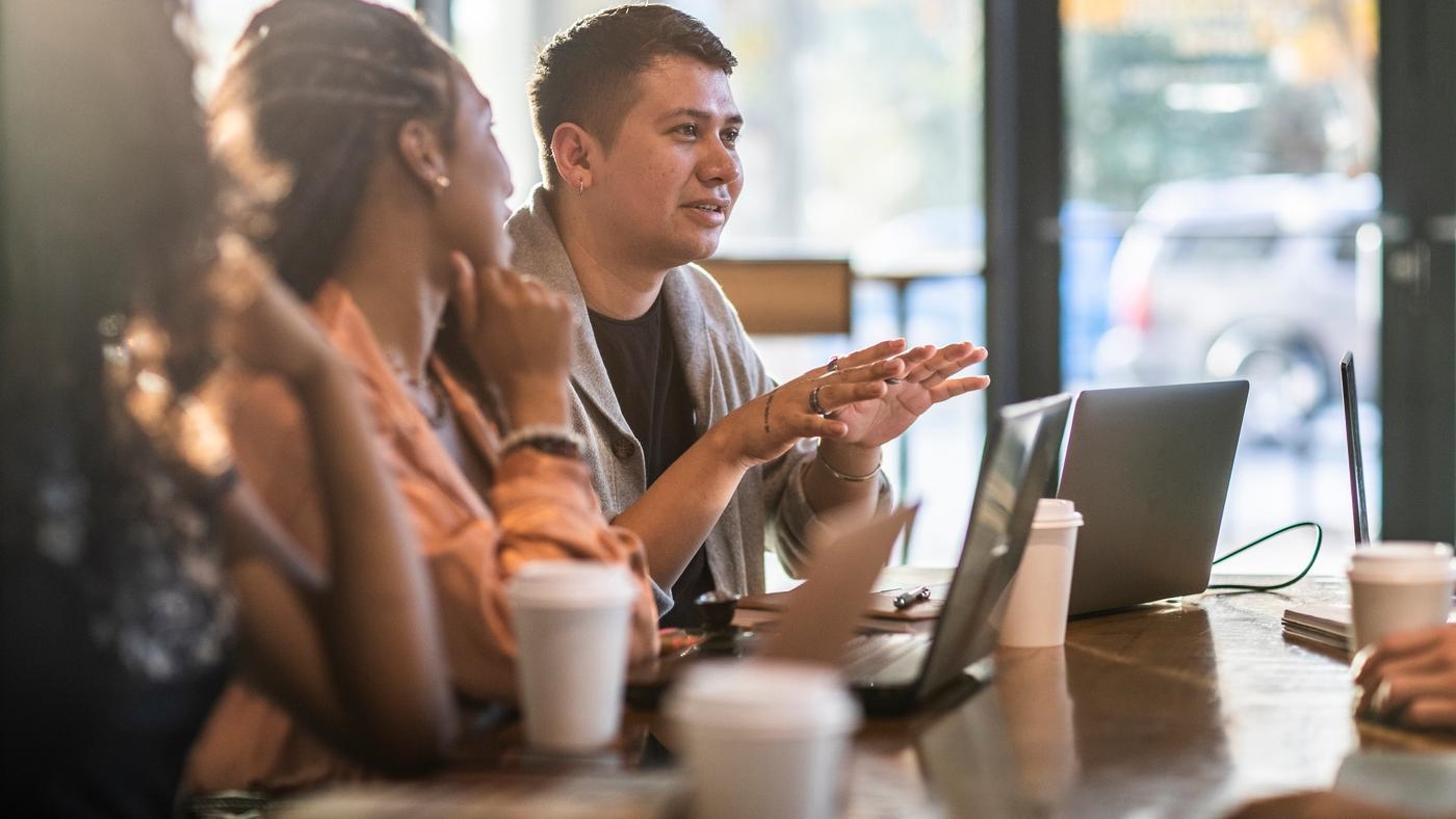 Young professionals collaborating in coffeeshop, laptops and coffees on the large table.