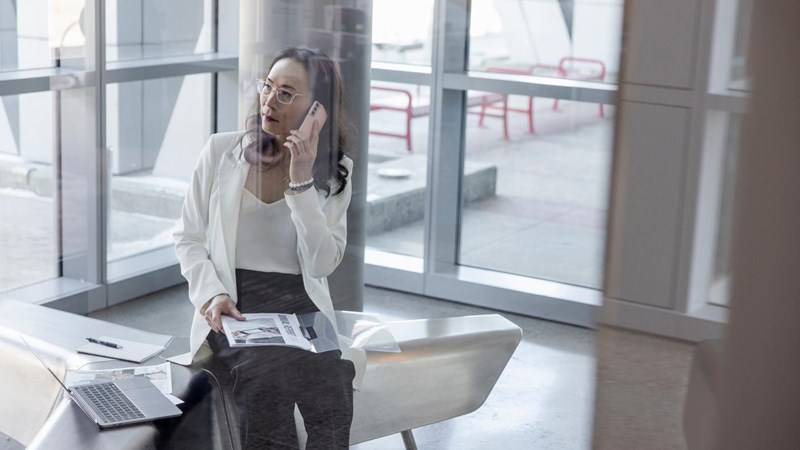Businesswoman with paperwork talking on smart phone in office lobby,