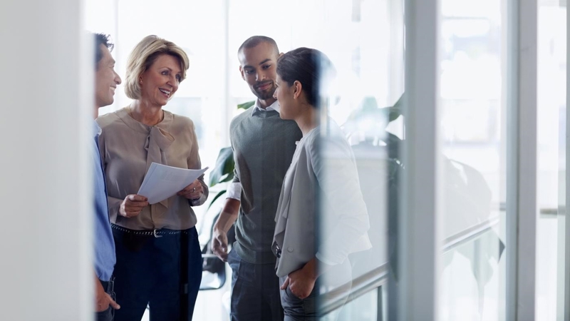 Smiling businesswoman discussing over document with colleagues in office.